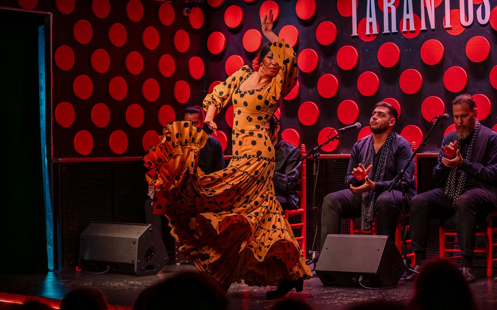 Flamenco dancer performing at Los Tarantos in Barcelona with musicians clapping.
