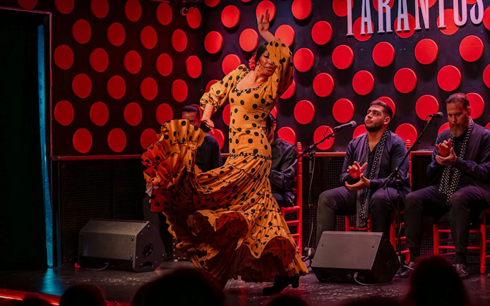 Flamenco dancer performing at Los Tarantos in Barcelona with musicians clapping.