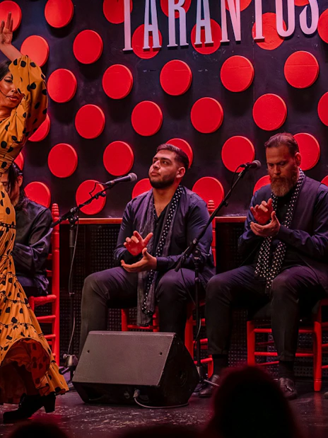 Flamenco dancer performing at Los Tarantos in Barcelona with musicians clapping.