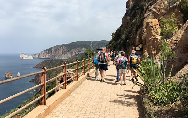 Hikers on the Faraglioni path from Nebida with coastal cliffs in view.