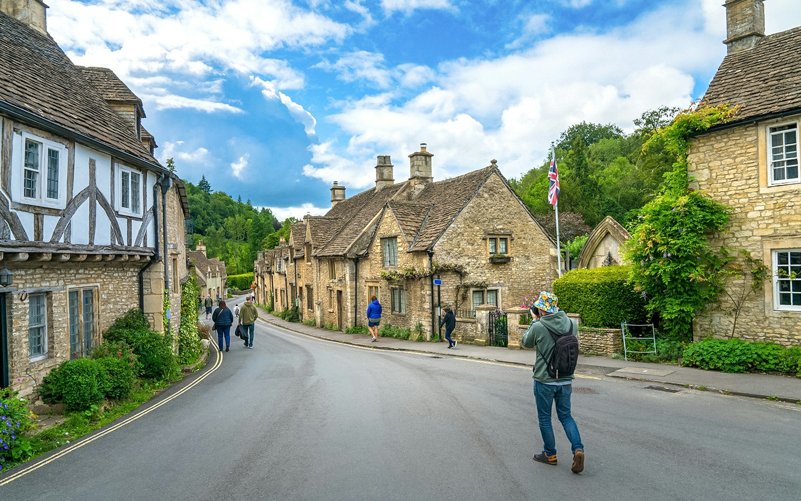 Quaint street in Castle Combe village, Cotswold, with historic stone cottages and visitors exploring.