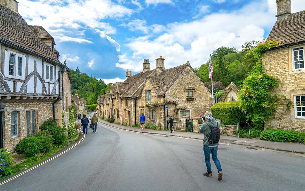 Quaint street in Castle Combe village, Cotswold, with historic stone cottages and visitors exploring.