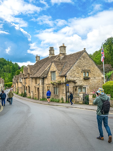 Quaint street in Castle Combe village, Cotswold, with historic stone cottages and visitors exploring.