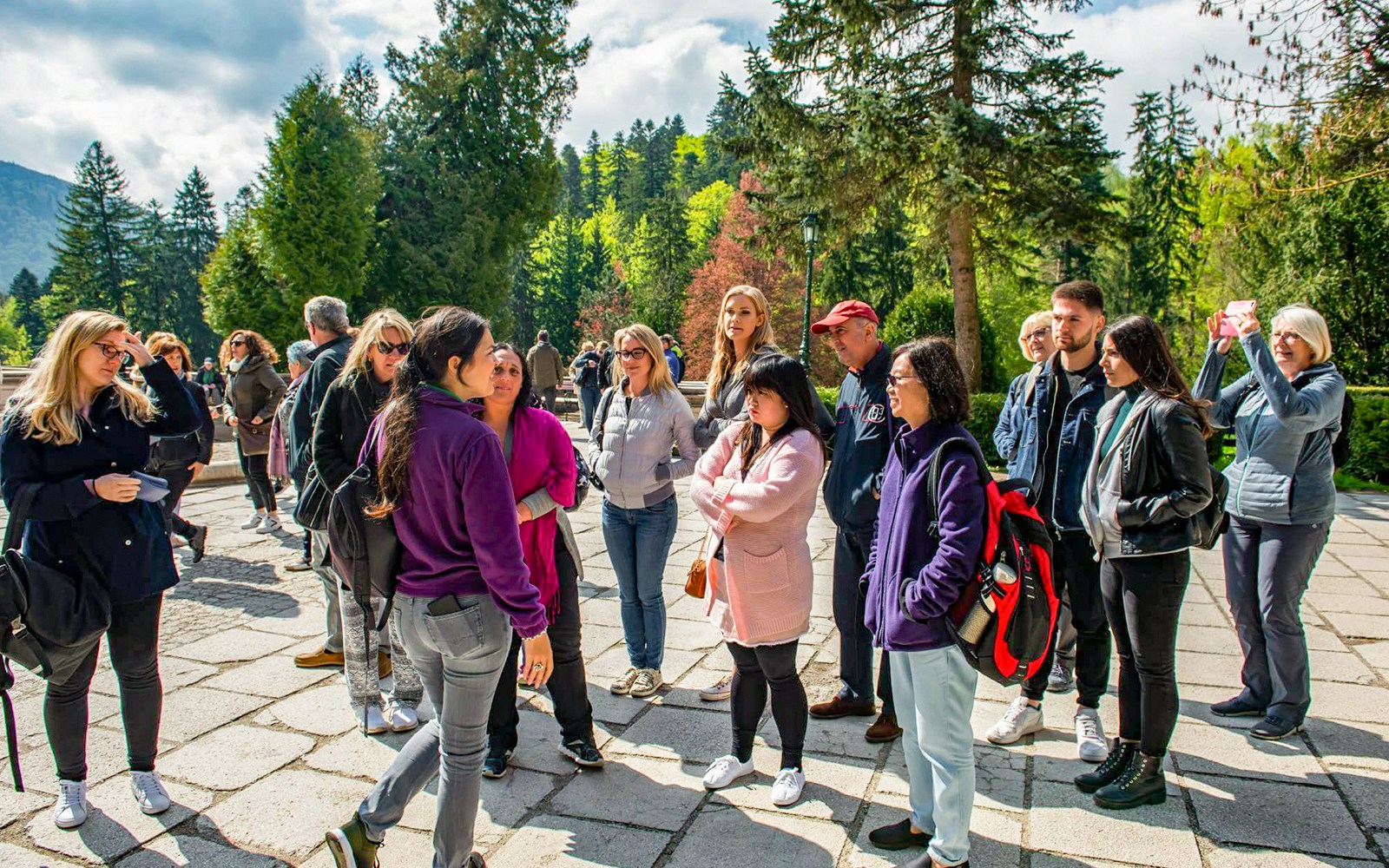 Group of tourists listening to a guide at Bran Castle, surrounded by lush greenery.