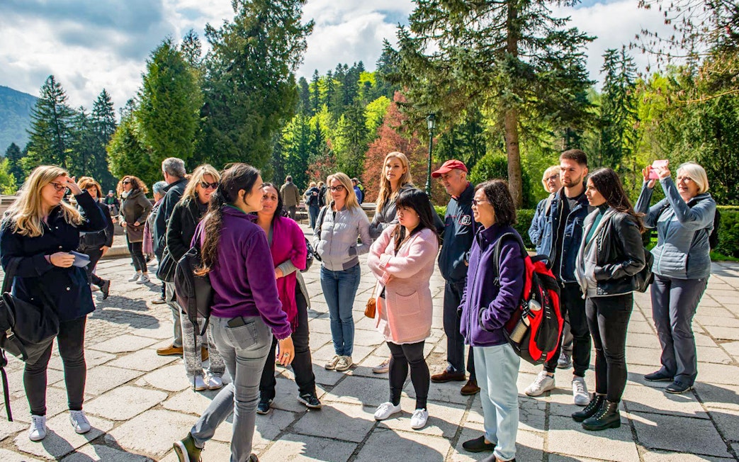 Group of tourists listening to a guide at Bran Castle, surrounded by lush greenery.