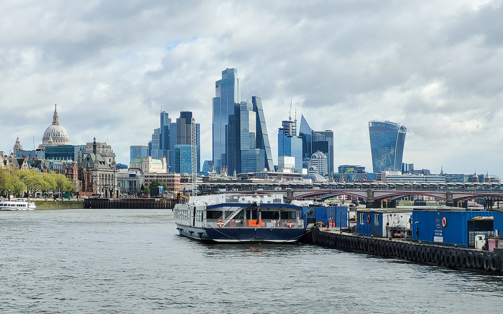 Cruise boat on the River Thames with London skyline, including St. Paul's Cathedral and modern skyscrapers.