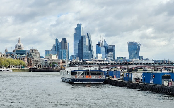 Cruise boat on the River Thames with London skyline, including St. Paul's Cathedral and modern skyscrapers.