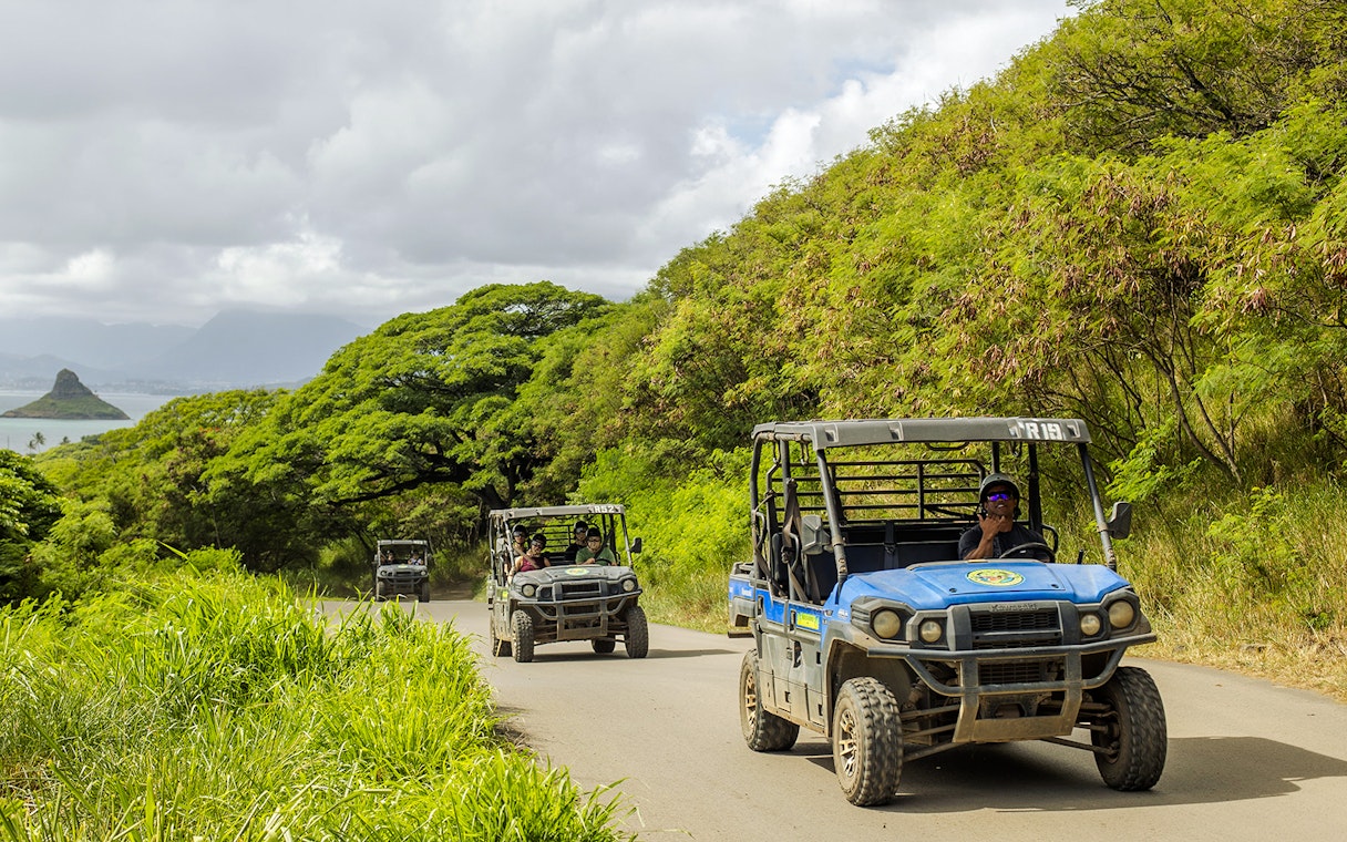 UTV Raptor vehicles on a scenic trail at Kualoa Ranch, Hawaii, with lush greenery and ocean view.