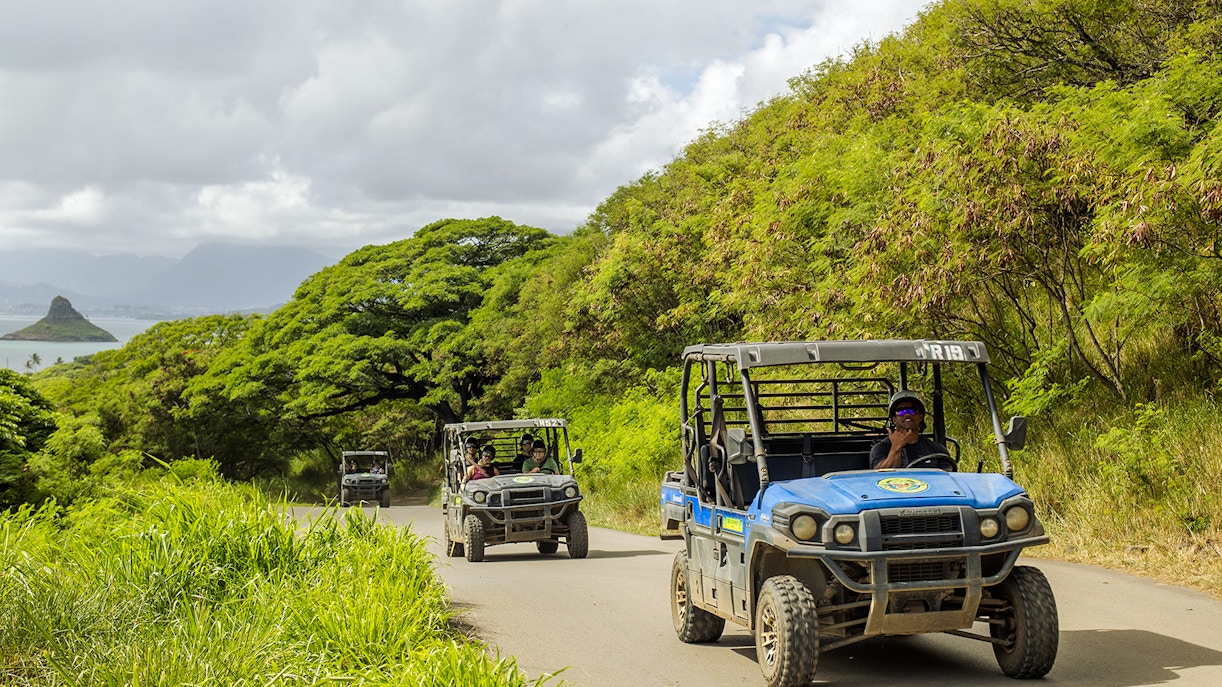 UTV Raptor vehicles on a scenic trail at Kualoa Ranch, Hawaii, with lush greenery and ocean view.