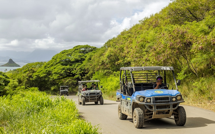 UTV Raptor vehicles on a scenic trail at Kualoa Ranch, Hawaii, with lush greenery and ocean view.