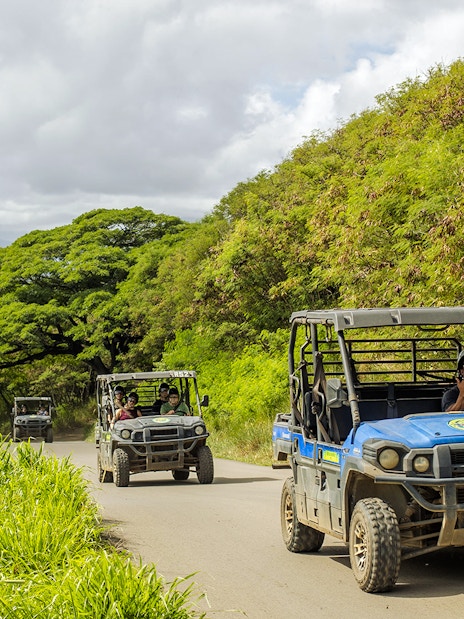 UTV Raptor vehicles on a scenic trail at Kualoa Ranch, Hawaii, with lush greenery and ocean view.
