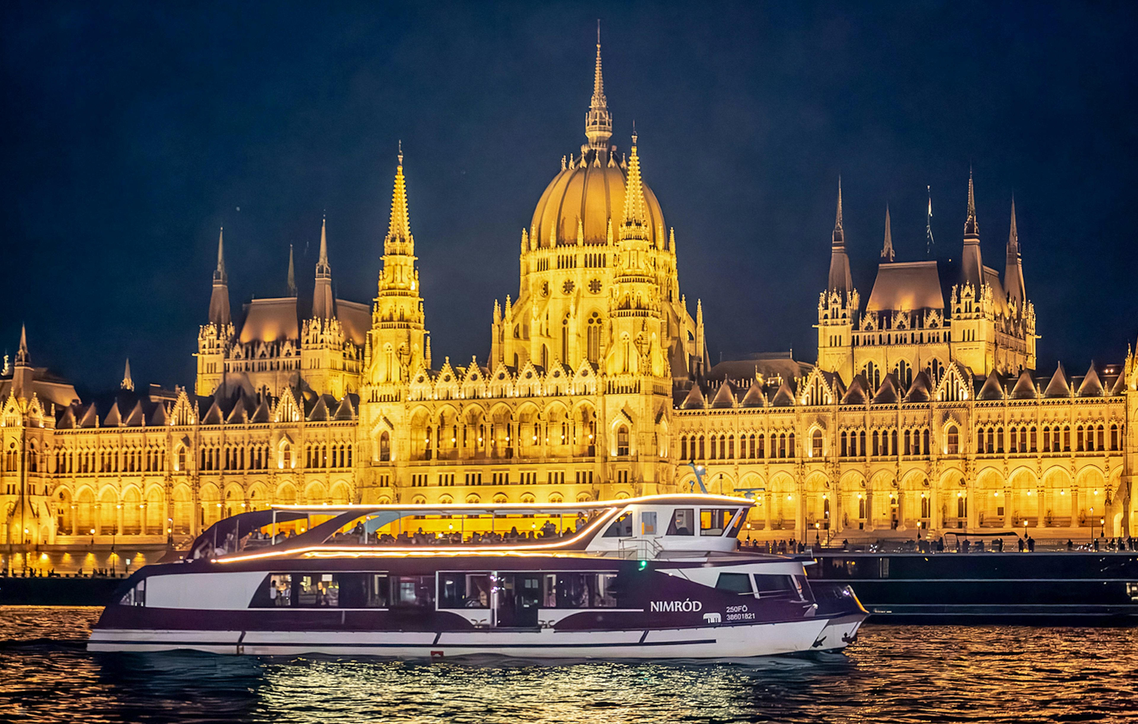 Cruise boat on the Danube River with Budapest Parliament illuminated at night.