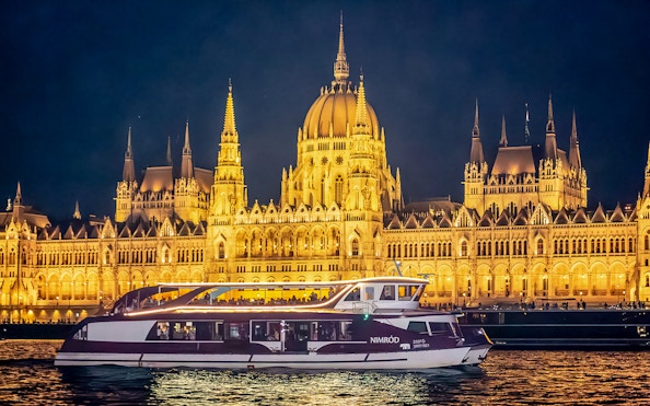 Cruise boat on the Danube River with Budapest Parliament illuminated at night.
