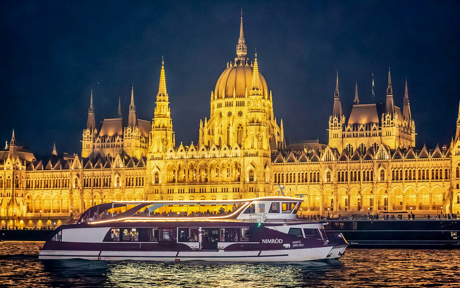 Cruise boat on the Danube River with Budapest Parliament illuminated at night.