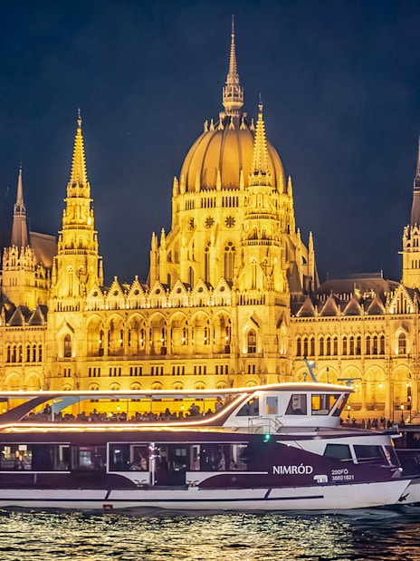 Cruise boat on the Danube River with Budapest Parliament illuminated at night.