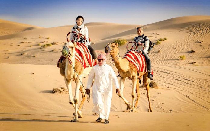 Camel ride in Abu Dhabi desert safari with guide leading two camels.