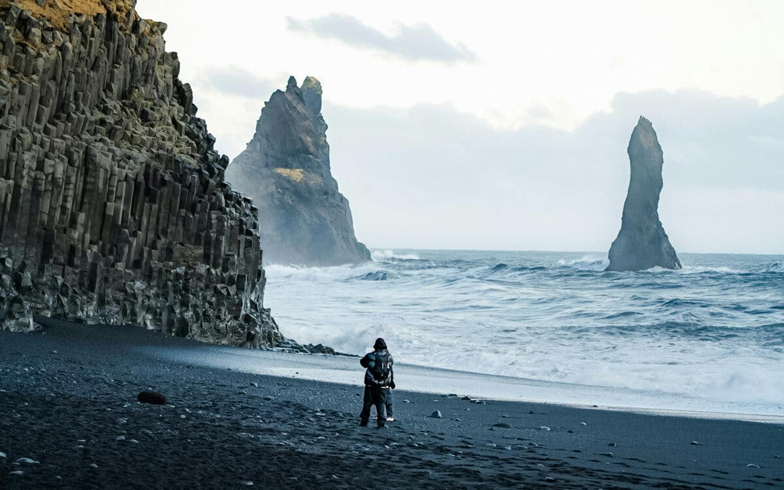 Guests walking on Reynisfjara Black Sand Beach with basalt columns and sea stacks in view.