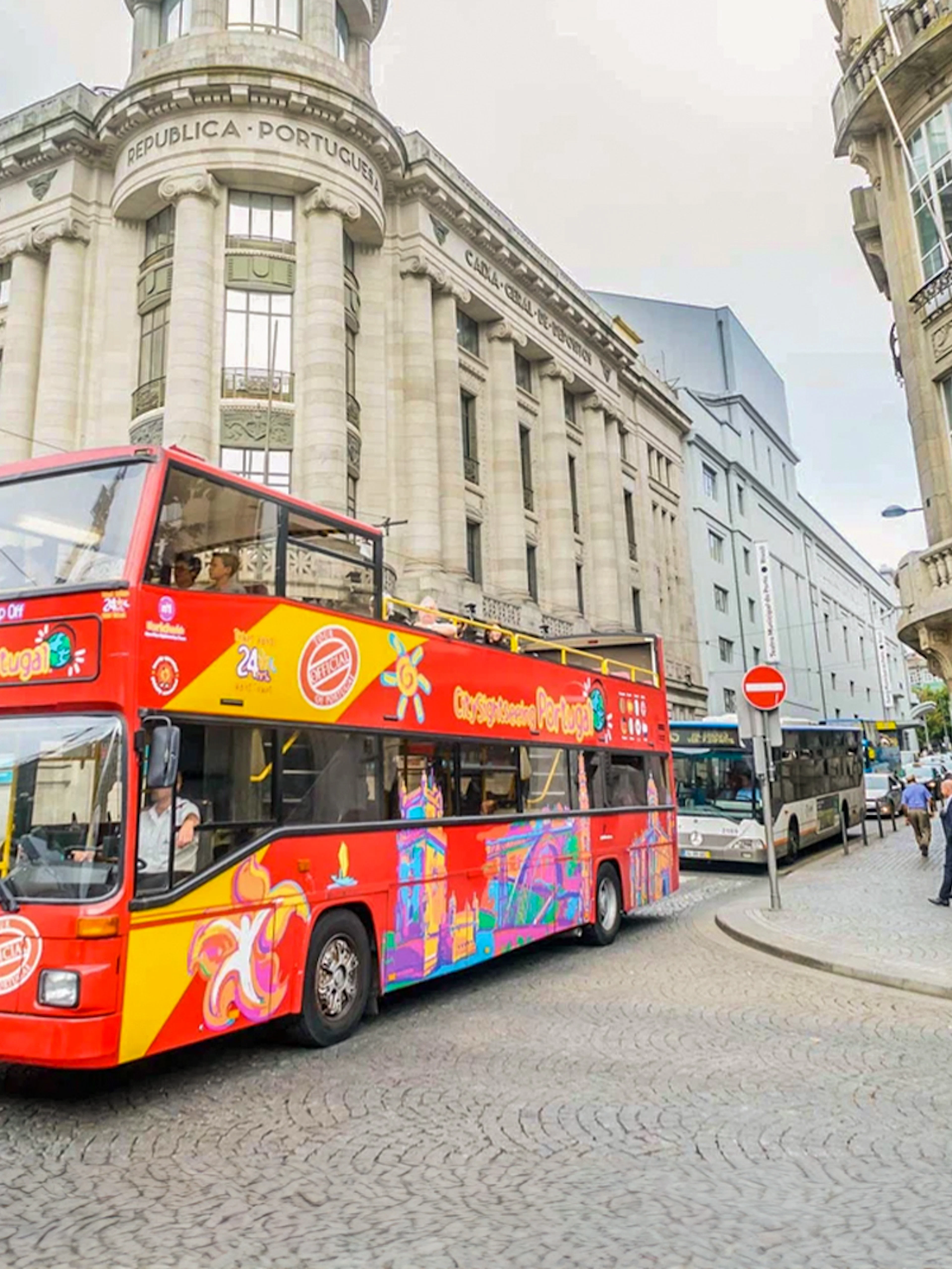 Red double-decker bus on a city tour in Porto, passing historic buildings.