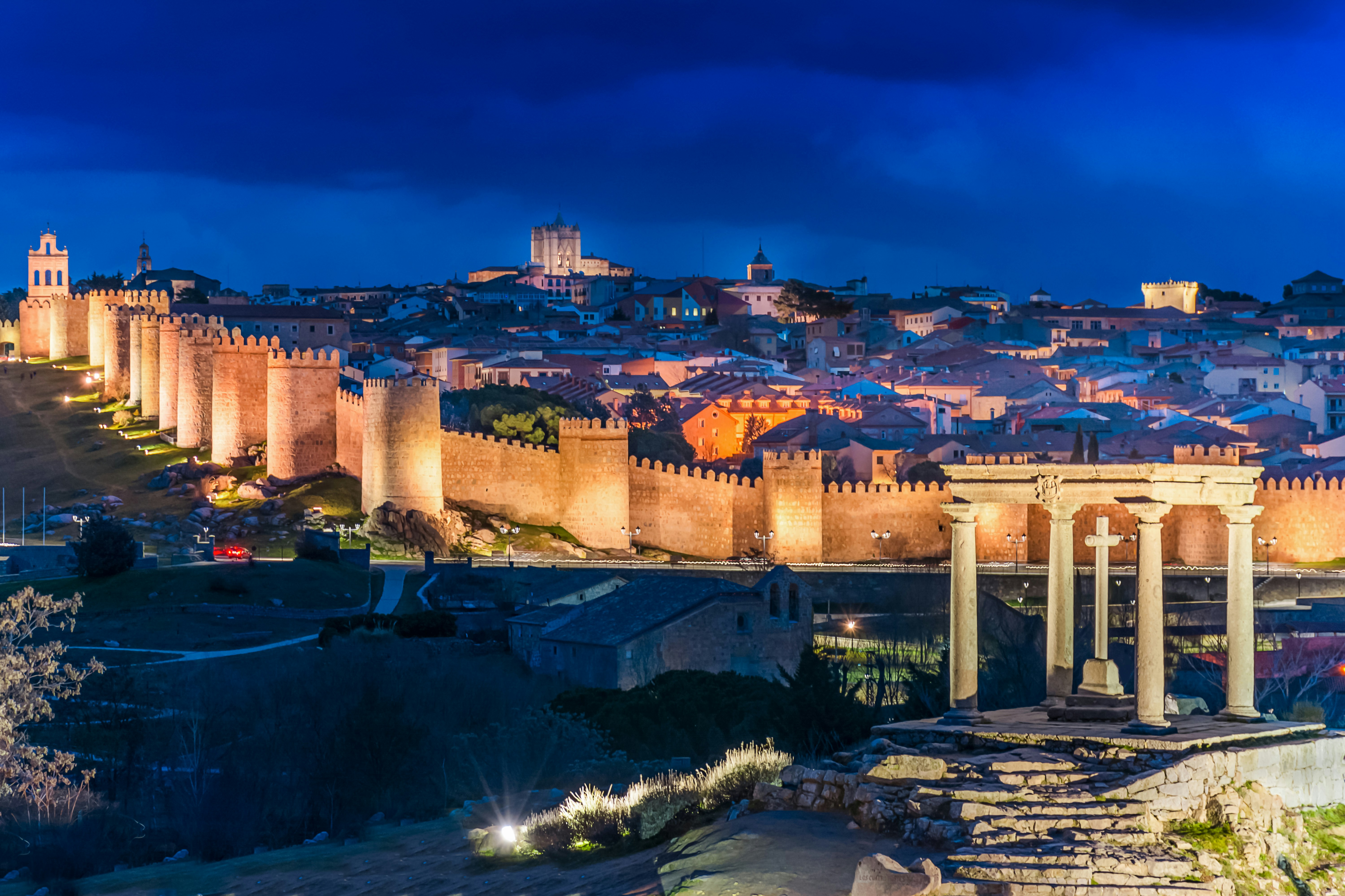 Walls of Ávila illuminated at night with cityscape in the background.