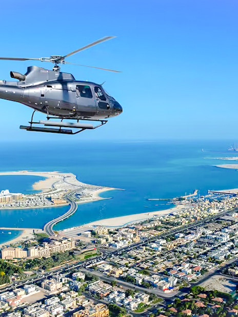 Helicopter flying over Dubai coastline with Palm Jumeirah in view.