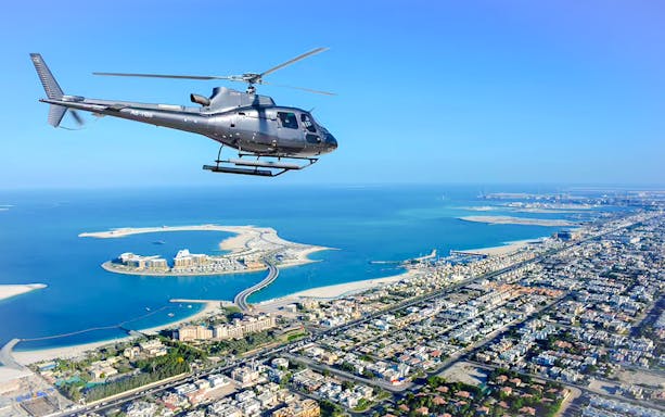 Helicopter flying over Dubai coastline with Palm Jumeirah in view.