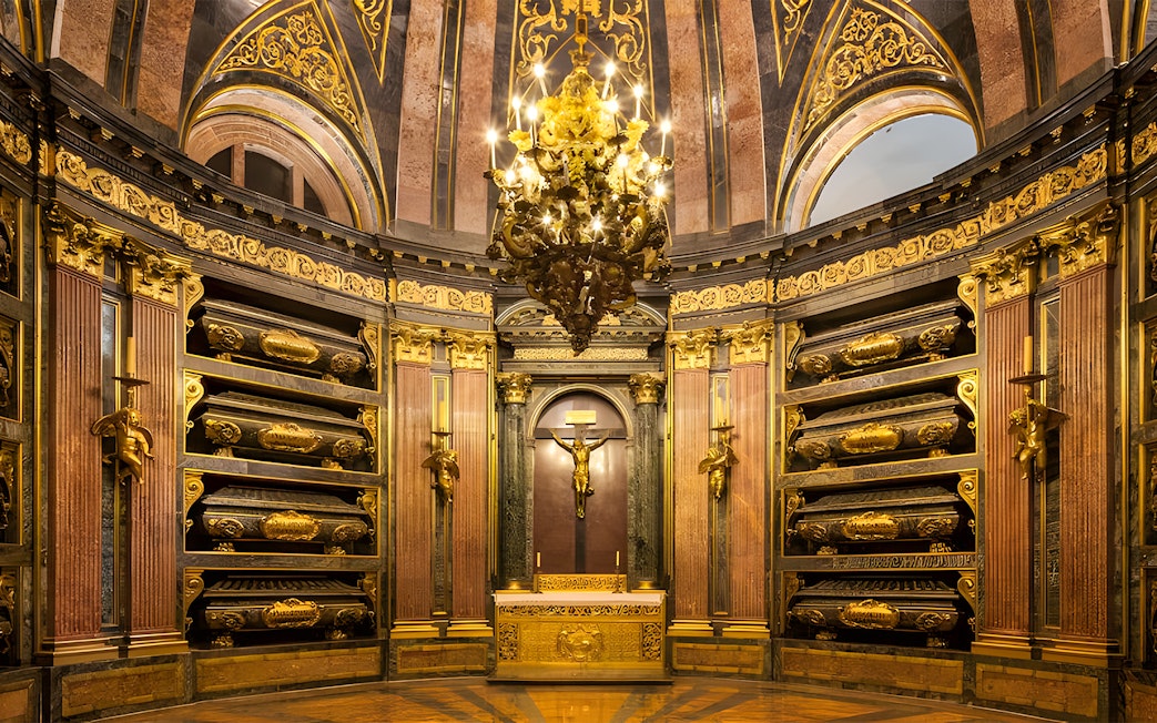 Royal Pantheon interior at San Lorenzo de El Escorial, featuring ornate gold details and tombs.