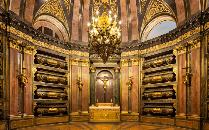 Royal Pantheon interior at San Lorenzo de El Escorial, featuring ornate gold details and tombs.