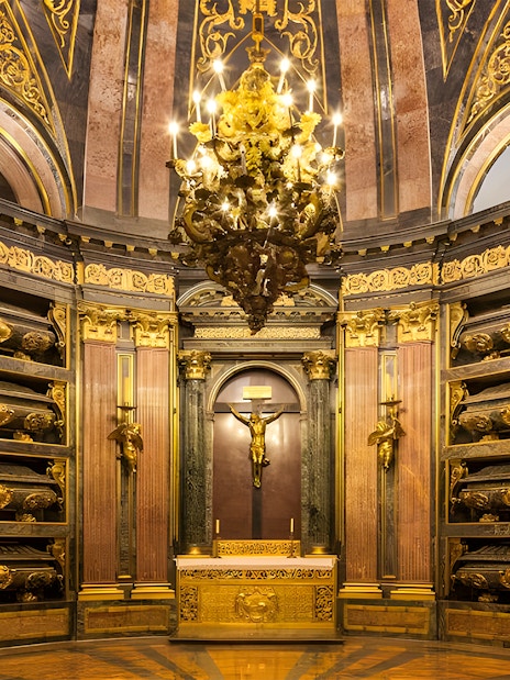 Royal Pantheon interior at San Lorenzo de El Escorial, featuring ornate gold details and tombs.