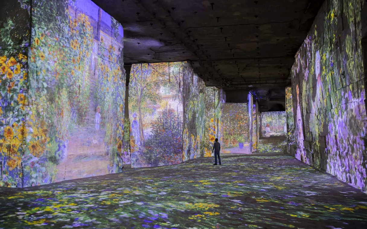 Monet's artwork projected on walls at Carrières des Lumières, person observing.