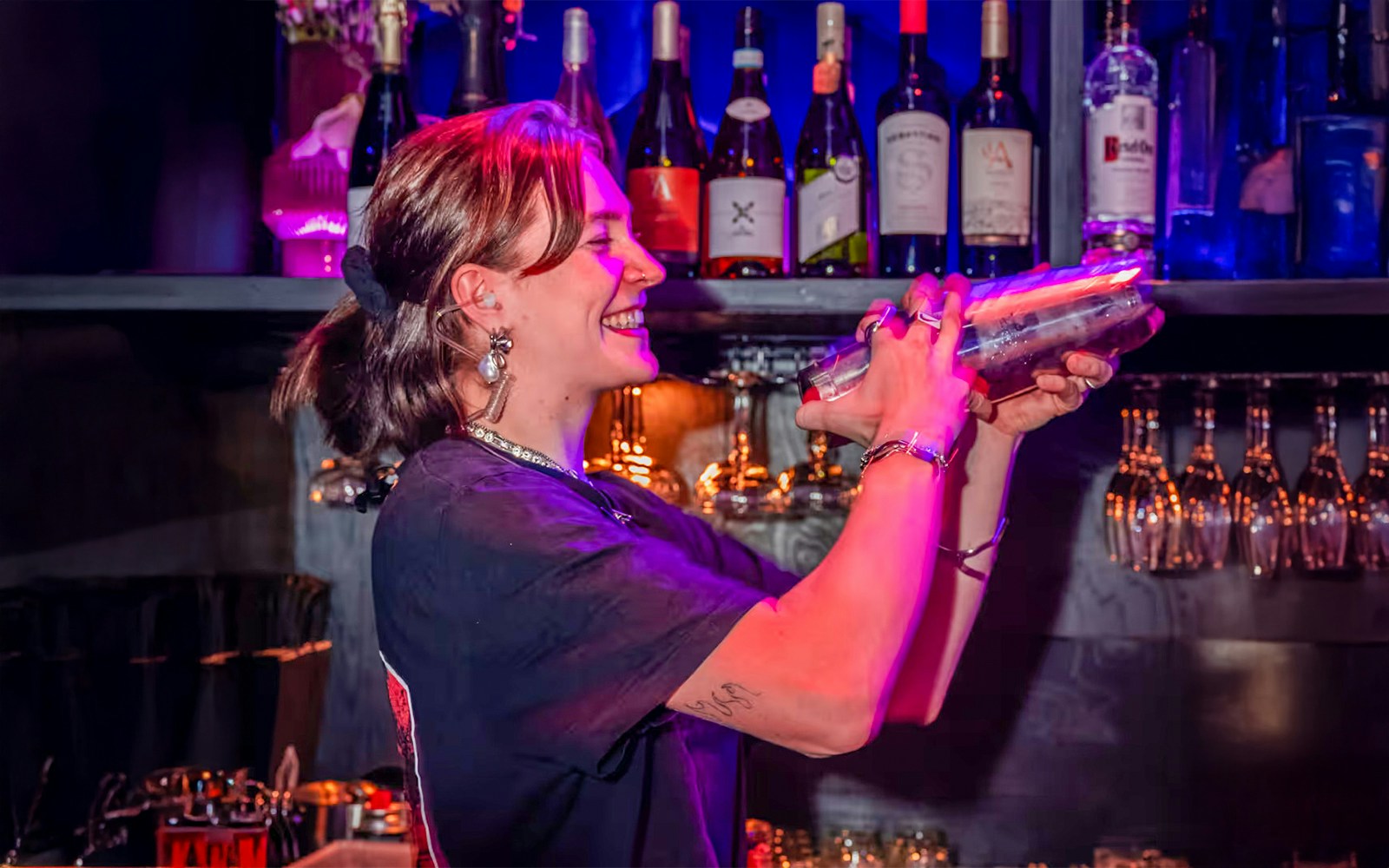 Bartender mixing drinks at Amaze Amsterdam with bottles and glasses in the background.
