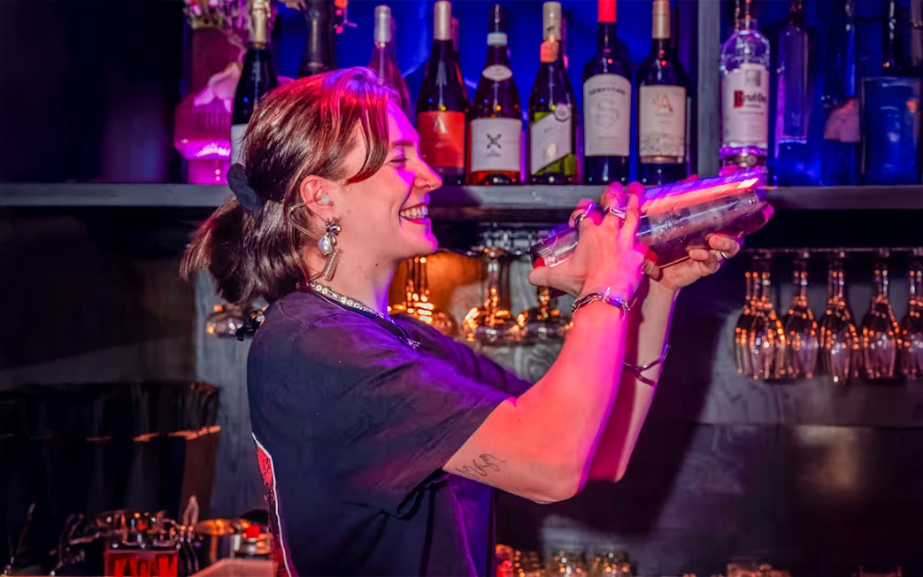 Bartender mixing drinks at Amaze Amsterdam with bottles and glasses in the background.