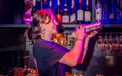 Bartender mixing drinks at Amaze Amsterdam with bottles and glasses in the background.