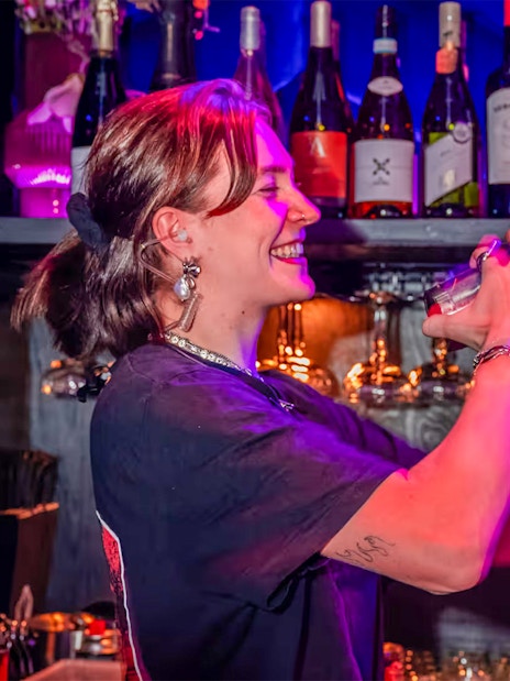 Bartender mixing drinks at Amaze Amsterdam with bottles and glasses in the background.