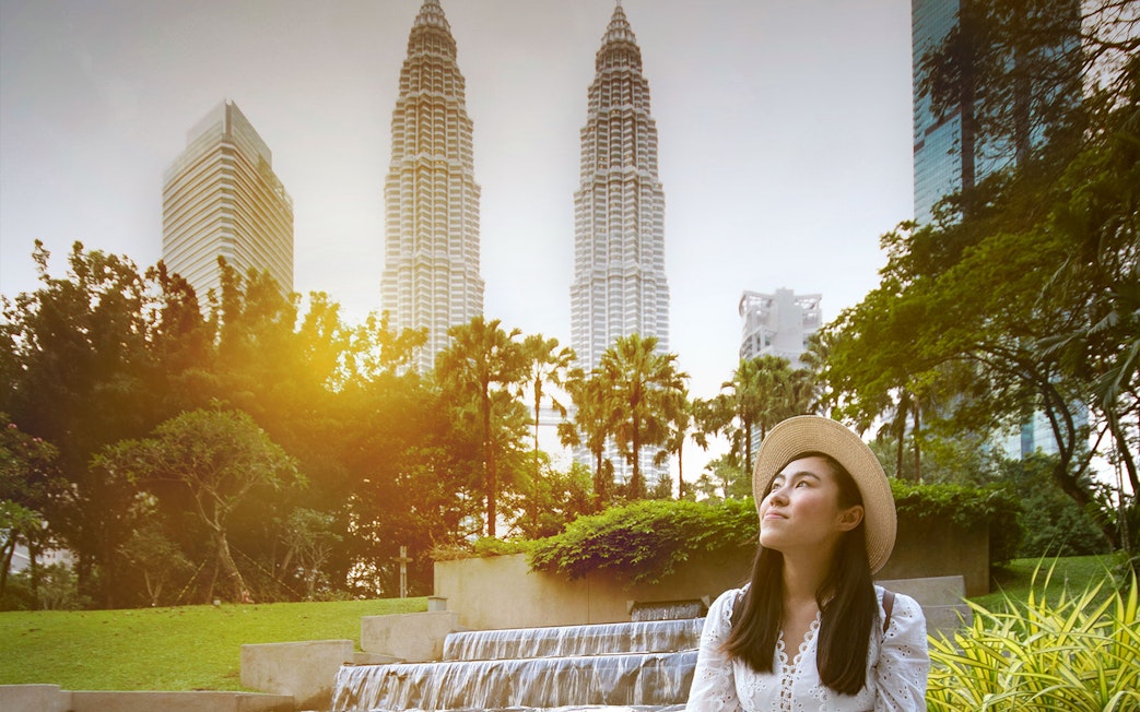 Woman in a hat posing in front of Kuala Lumpur's Petronas Towers.