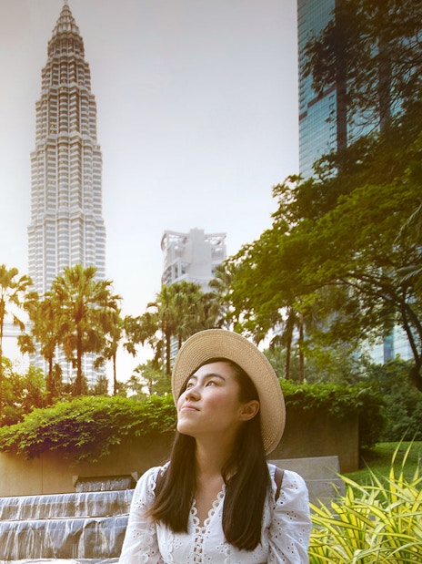 Woman in a hat posing in front of Kuala Lumpur's Petronas Towers.