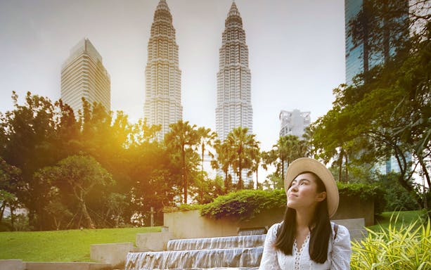 Woman in a hat posing in front of Kuala Lumpur's Petronas Towers.