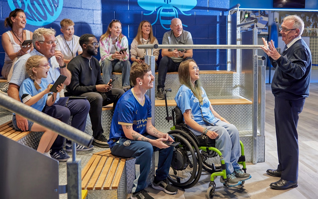 Group enjoying a guided tour at Manchester City Stadium, listening to a guide.