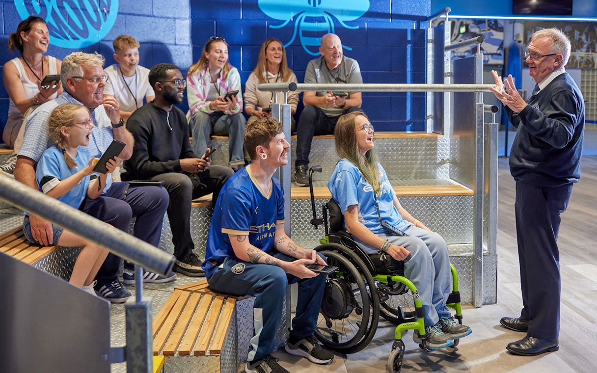 Group enjoying a guided tour at Manchester City Stadium, listening to a guide.