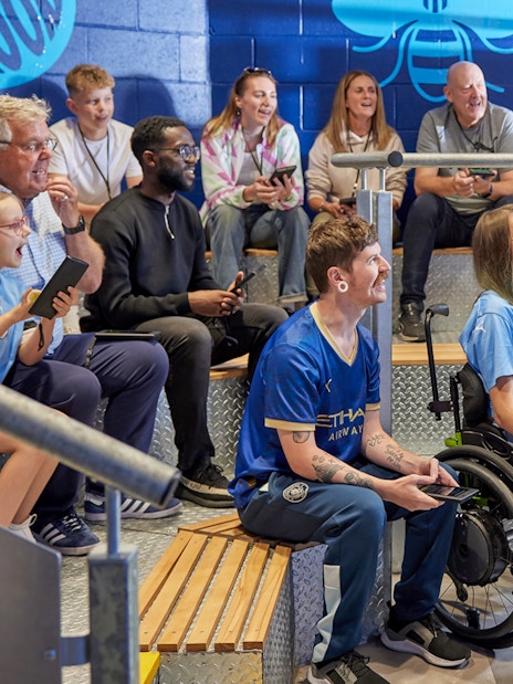 Group enjoying a guided tour at Manchester City Stadium, listening to a guide.