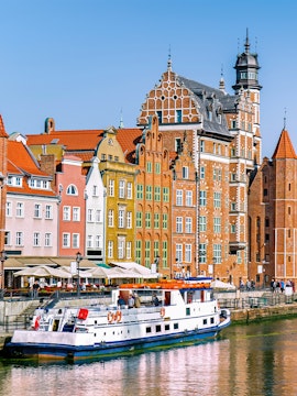 Cruise boat on Motława River with colorful historic buildings in Gdansk, Poland.