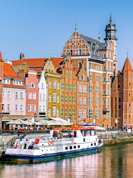 Cruise boat on Motława River with colorful historic buildings in Gdansk, Poland.