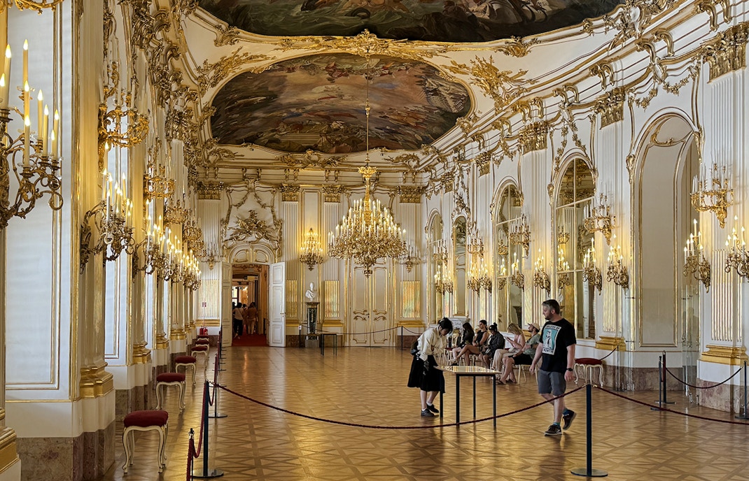 Great Gallery inside Schönbrunn Palace, Vienna with ornate chandeliers and visitors exploring.