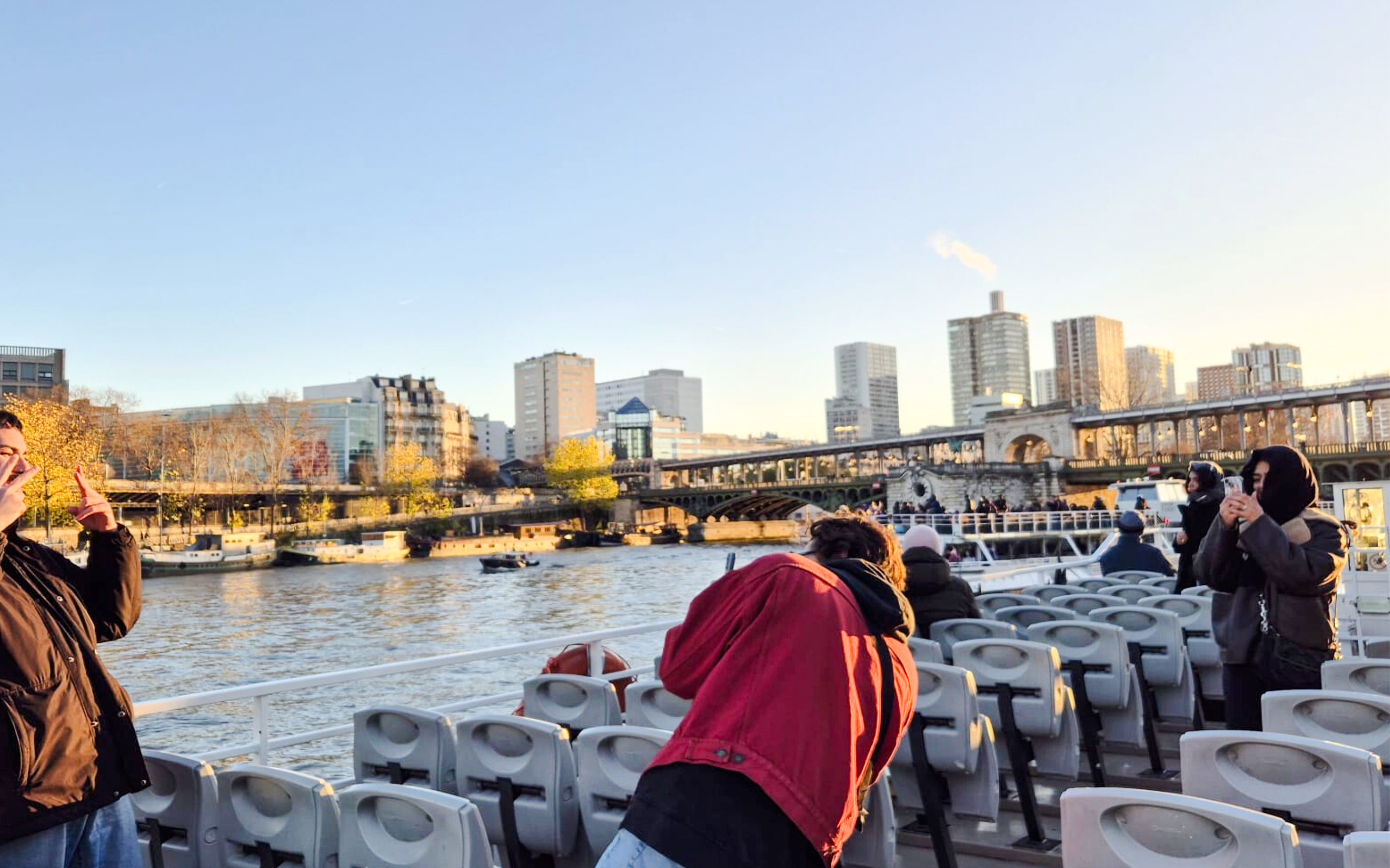 People taking photos on a Seine River cruise with Paris skyline in the background.