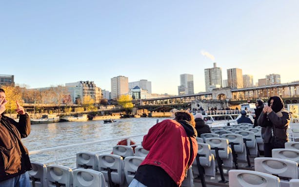 People taking photos on a Seine River cruise with Paris skyline in the background.