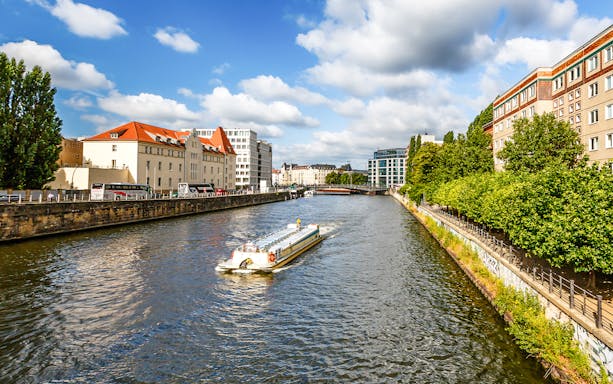 Boat cruising on the Spree River in Berlin, surrounded by city buildings and trees.