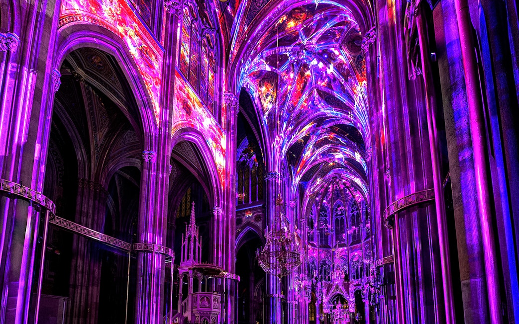 Vibrant light display inside Votivkirche, Vienna, showcasing colorful illuminated arches.