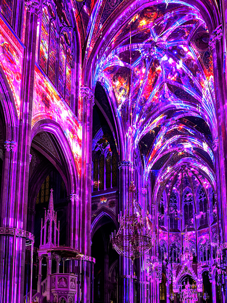 Vibrant light display inside Votivkirche, Vienna, showcasing colorful illuminated arches.