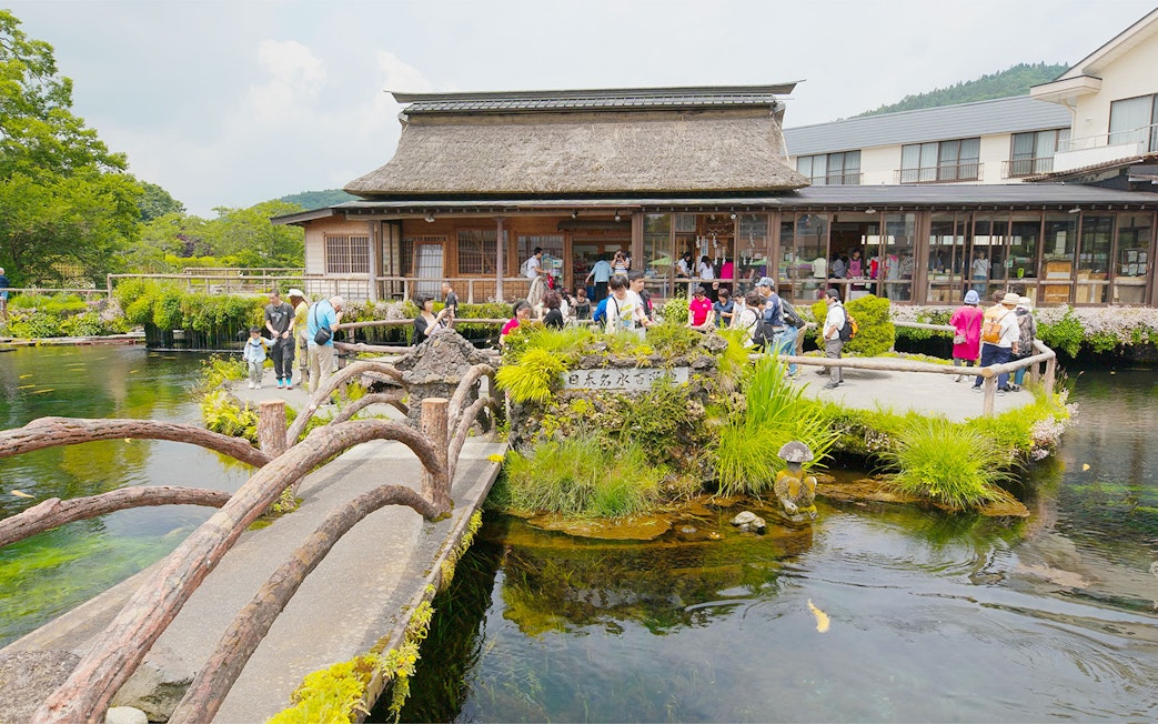 Visitors exploring Oshino Hakkai's sacred ponds with traditional Japanese architecture in the background.