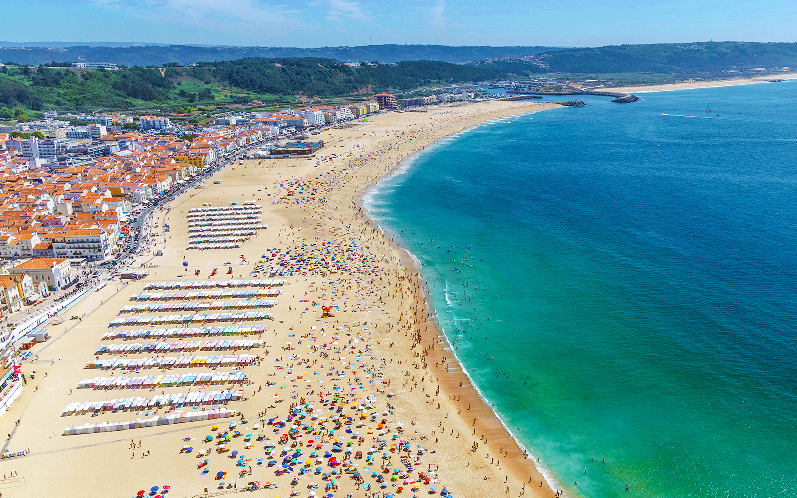 Nazaré beach crowded with people and colorful umbrellas on a summer day, Portugal.