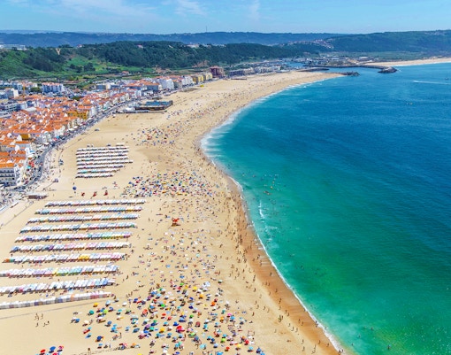 Nazaré beach crowded with people and colorful umbrellas on a summer day, Portugal.